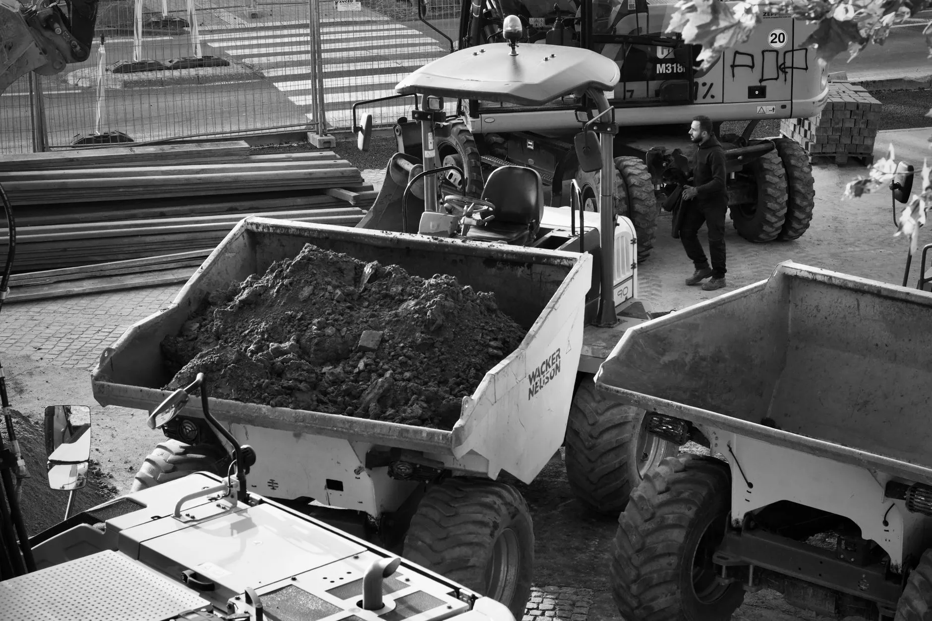 A worker beside a loaded dump truck on a job site.